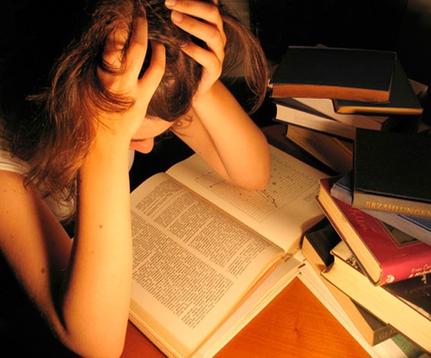 Estudiante estresado estudiando rodeado de libros